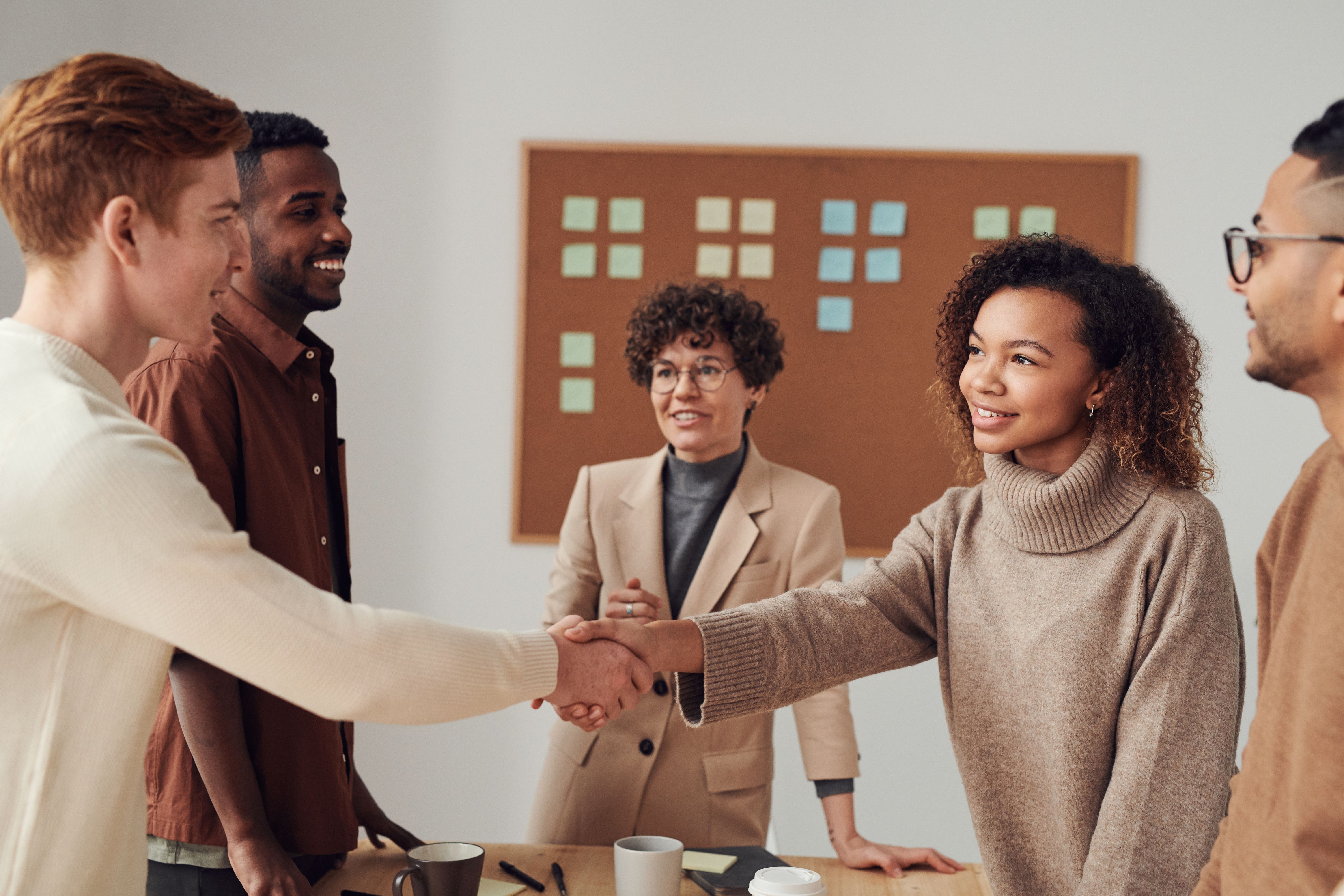Five diverse colleagues smiling as two shake hands in an office