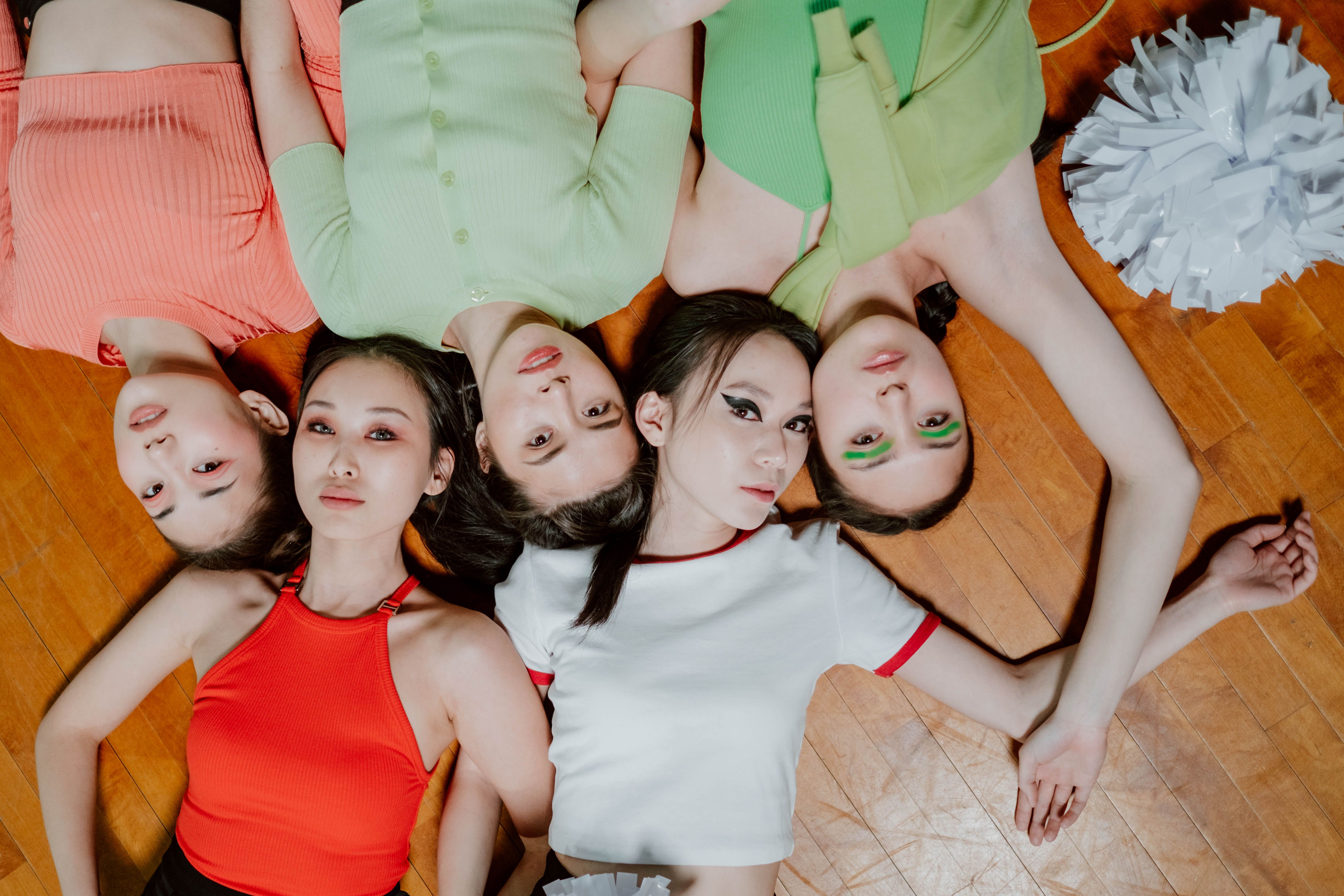 K-pop group members in colorful outfits lying on a wooden floor